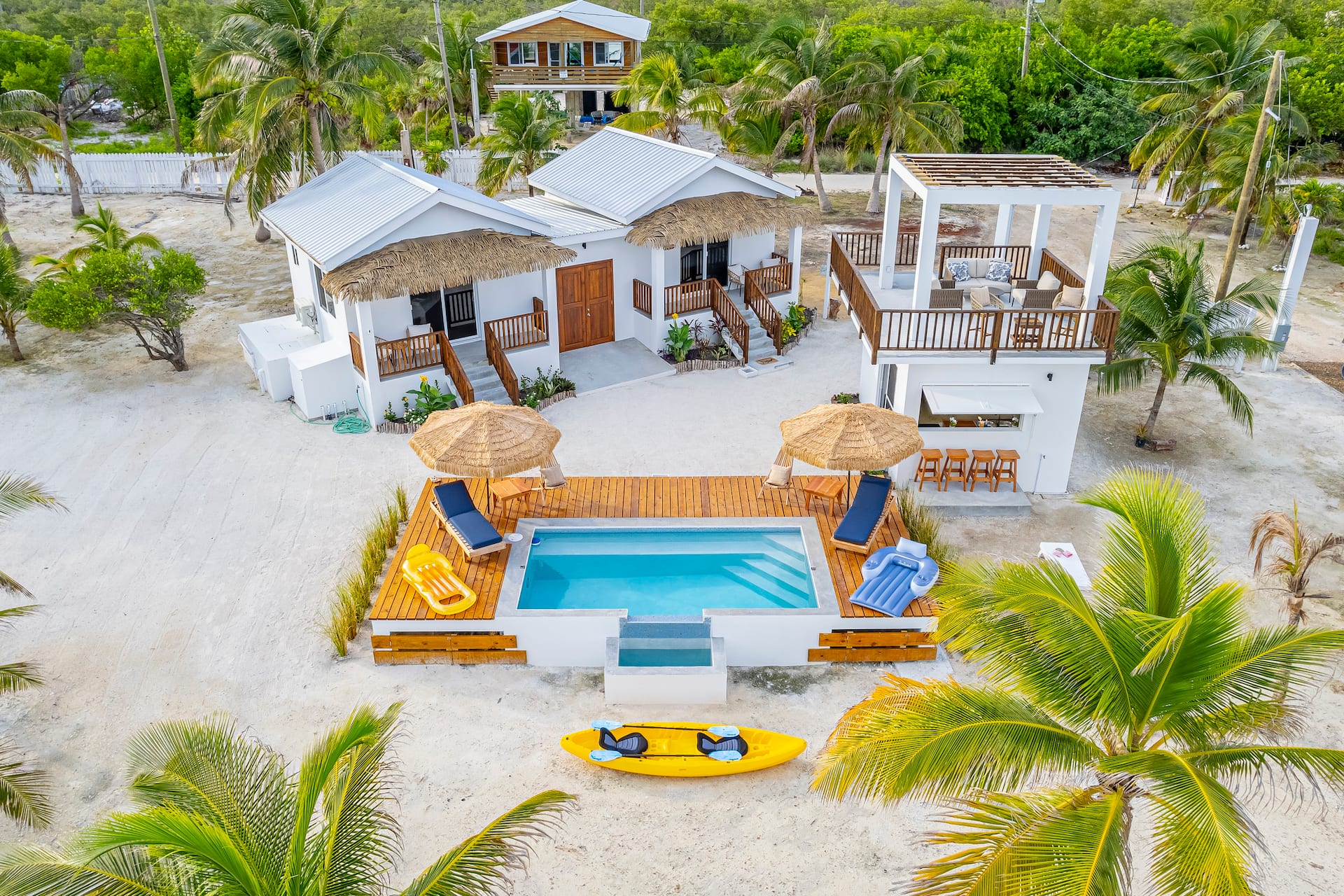 Aerial view of the two white casitas facing the pool, with yellow kayaks on the sand and palm trees around