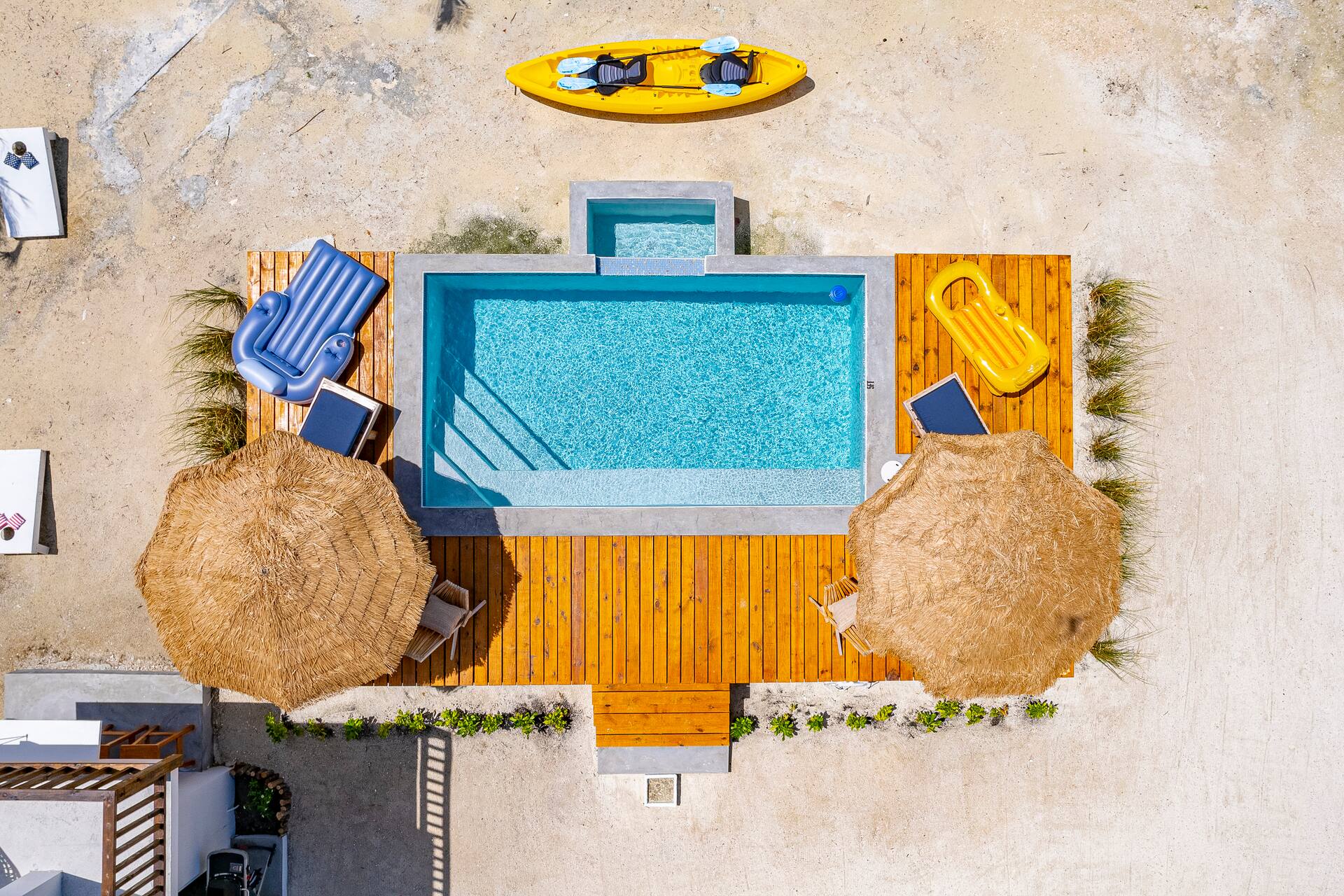 Overhead view of the turquoise pool with wooden deck, loungers and thatched umbrellas